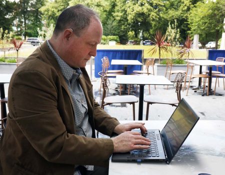 Phil Creighton at an open air cafe typing a review on a laptop