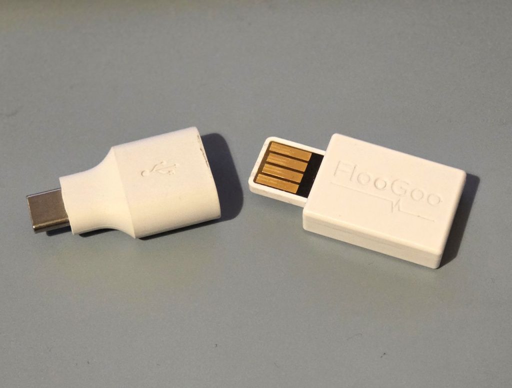 The FlooGoo FMA120 Auracast dongle next to a USB A to USB C converter