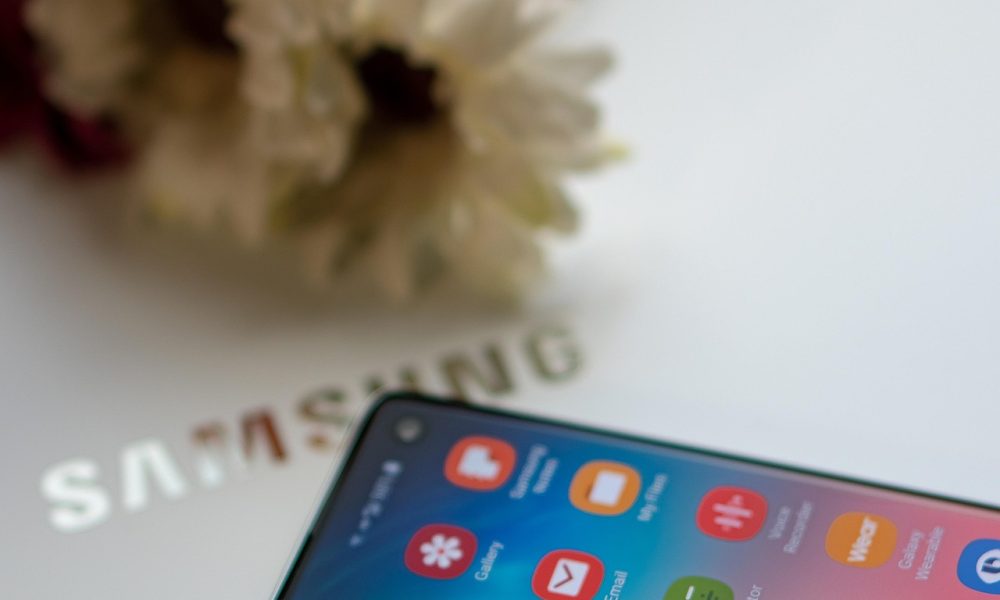 Samsung One UI 8 beta has launched. Picture shows a Samsung mobile phone on a Samsung laptop screen with some flowers in the background