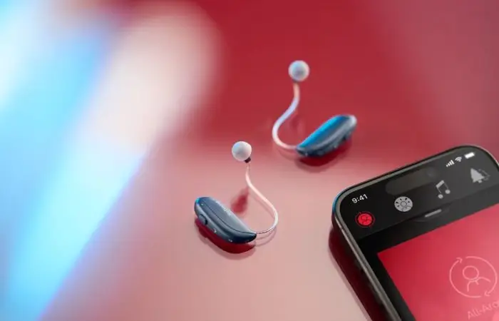 The ReSound Vivia hearing aids on a red background. On the right hand side of the image is a mobile phone showing the ReSound app