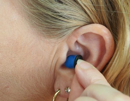 A person inserting a hearing aid into their ear. We do not know if they have Auracast in the ear. the RNID wants to see Auracast adopted by hearing aid manufacturers