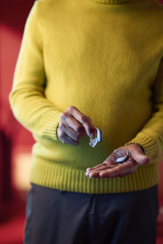 A person holding a ReSound Enzo IA hearing aid in each hand. They are wearing a yellow jumper
