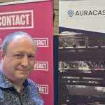 Phil Creighton standing next to a banner saying CONTACT and a banner with the Auracast Logo