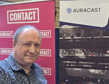 Phil Creighton standing next to a banner saying CONTACT and a banner with the Auracast Logo