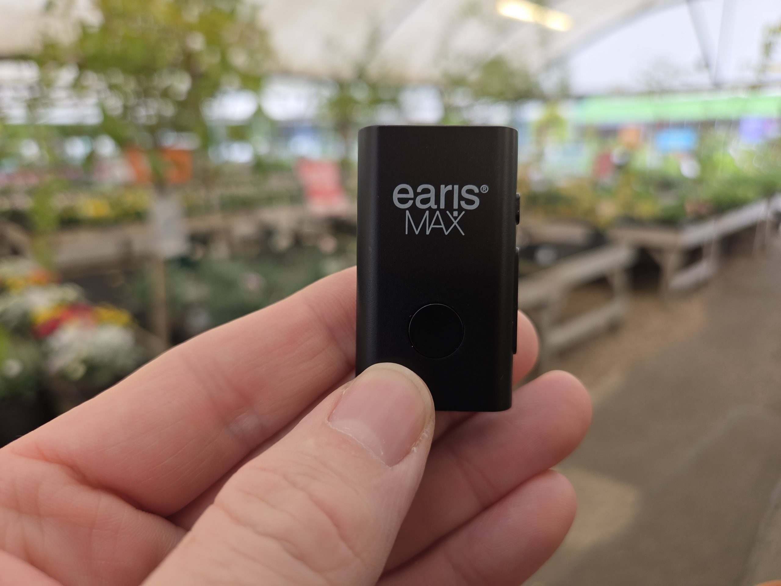 earisMAX Auracast streaming microphone held between finger and thumb in a garden centre