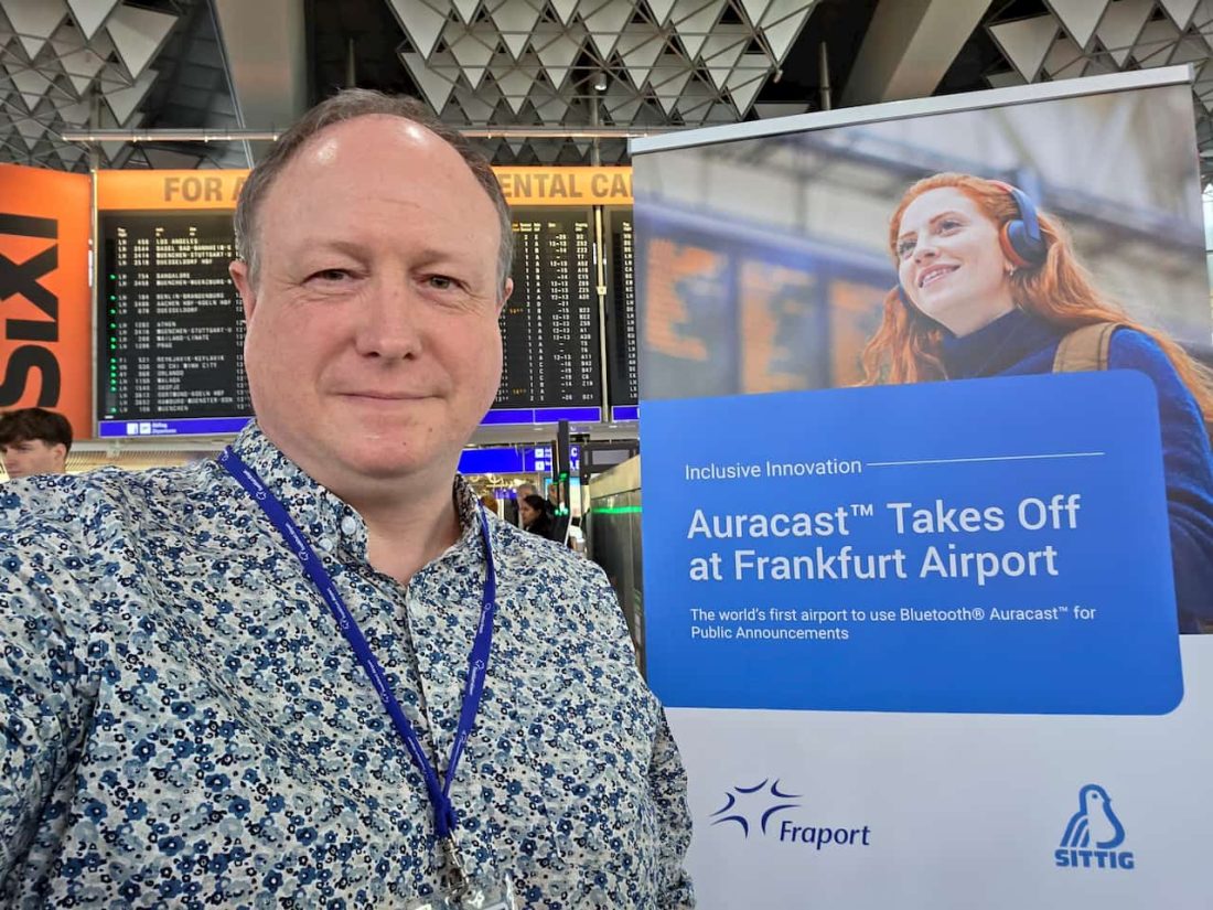 Phil Creighton at Frankfurt Airport next to a banner announced the launch of Auracast