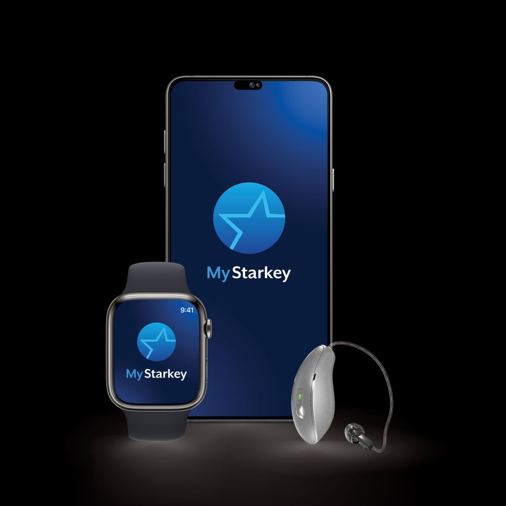 A mobile phone, a smartwatch and a Starkey hearing aid against a black background