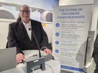 A man standing at a desk with an Auracast-enabled public address system in front of him. A banner is behind him